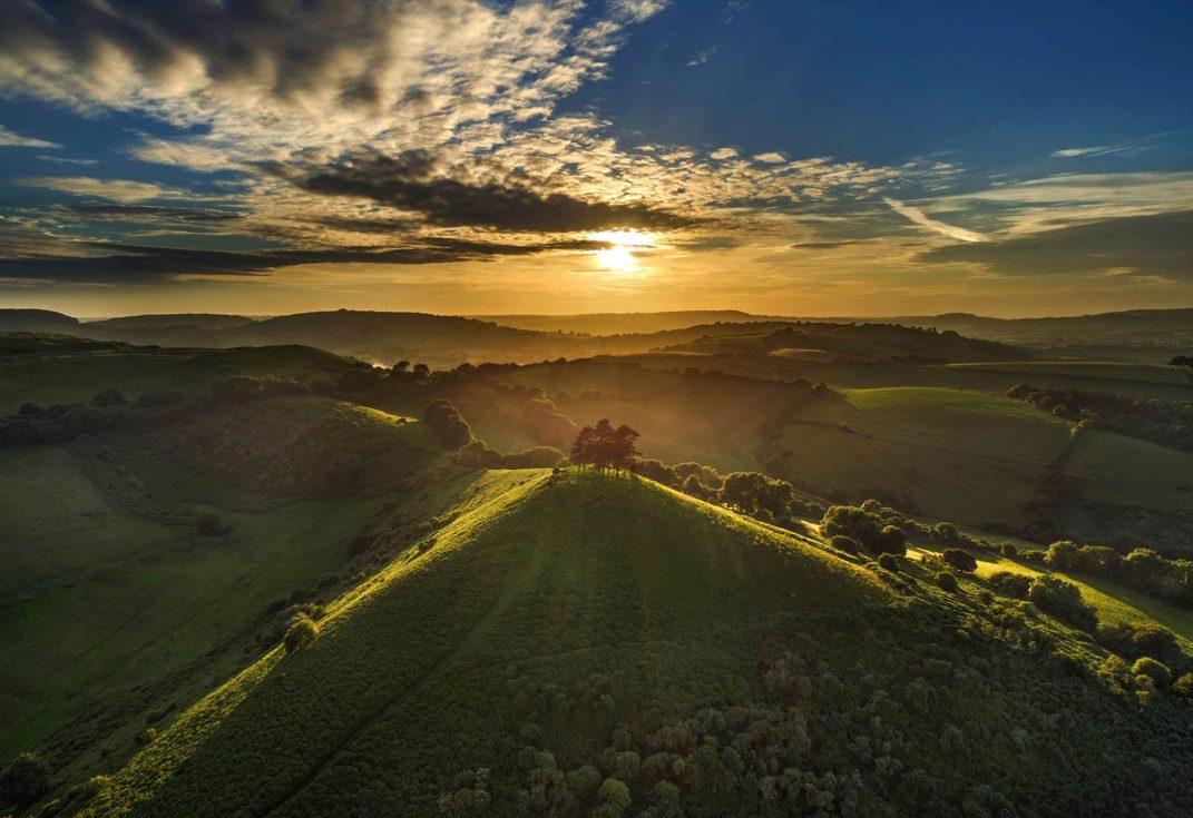 View from above of Colmers Hill with sunset light on the tops of the hills and surrounding fields and woods in early evening shadow
