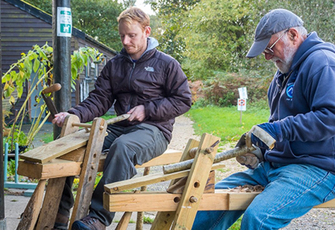 Two men sitting in a courtyard using equipment to work with wood