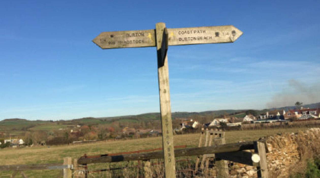 Wooden fingerpost post in a field with hills in the background and blue sky