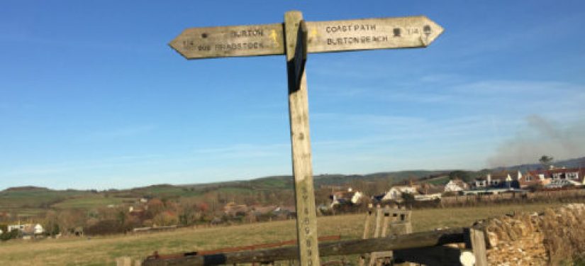 Wooden fingerpost post in a field with hills in the background and blue sky