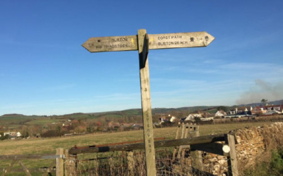 Wooden fingerpost post in a field with hills in the background and blue sky
