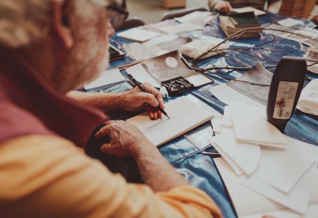 Man sketching twigs on a table filled with art materials