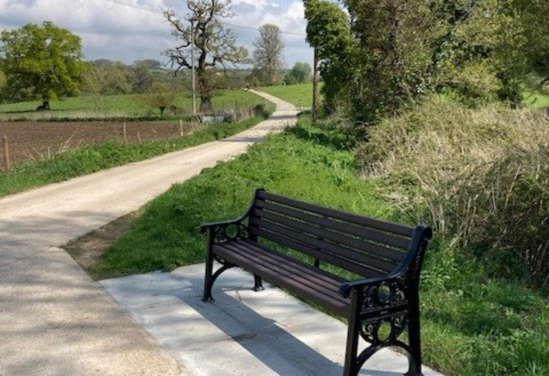 Park bench next to a wide path running alongside fields and woods