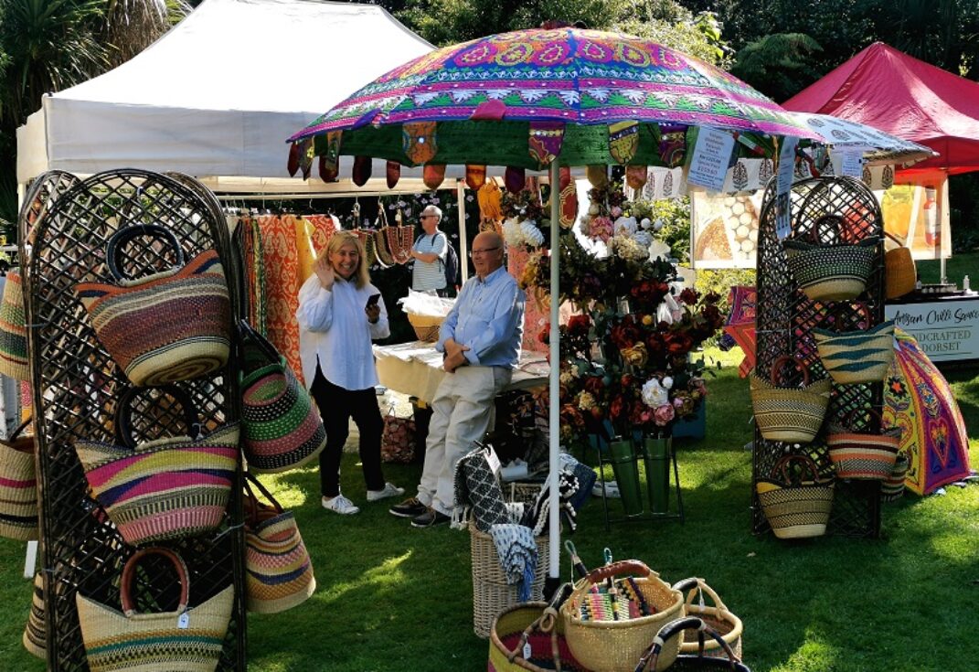 A craft stall selling brightly coloured baskets in a field on a sunny day