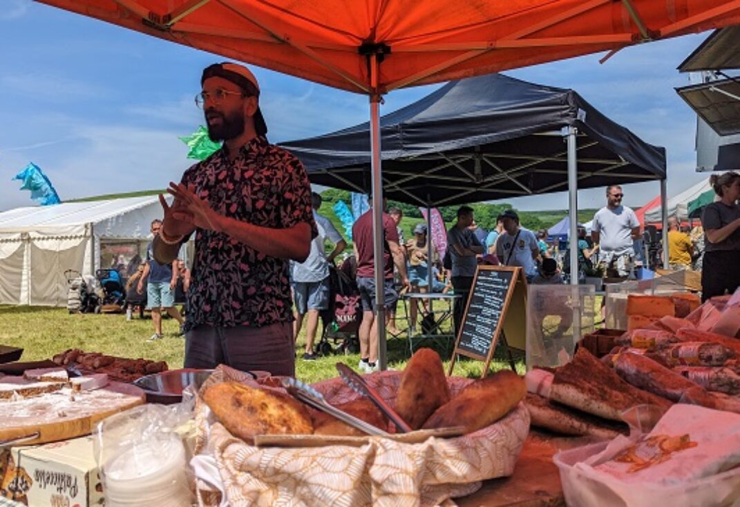 A food festival on a sunny day with stall holders talking to customers