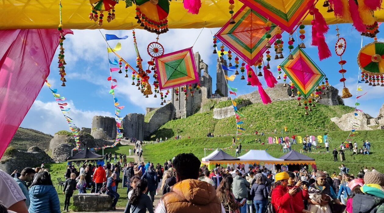 Bright flags waving at Corfe Castle ruins for a festival with a large crowd of people in the foreground
