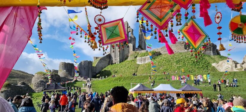 Bright flags waving at Corfe Castle ruins for a festival with a large crowd of people in the foreground