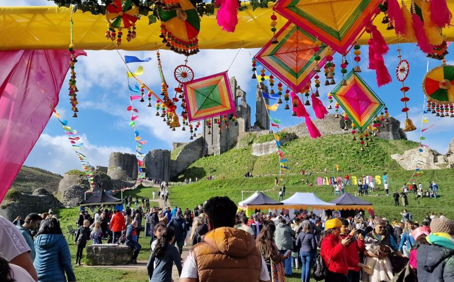 Bright flags waving at Corfe Castle ruins for a festival with a large crowd of people in the foreground