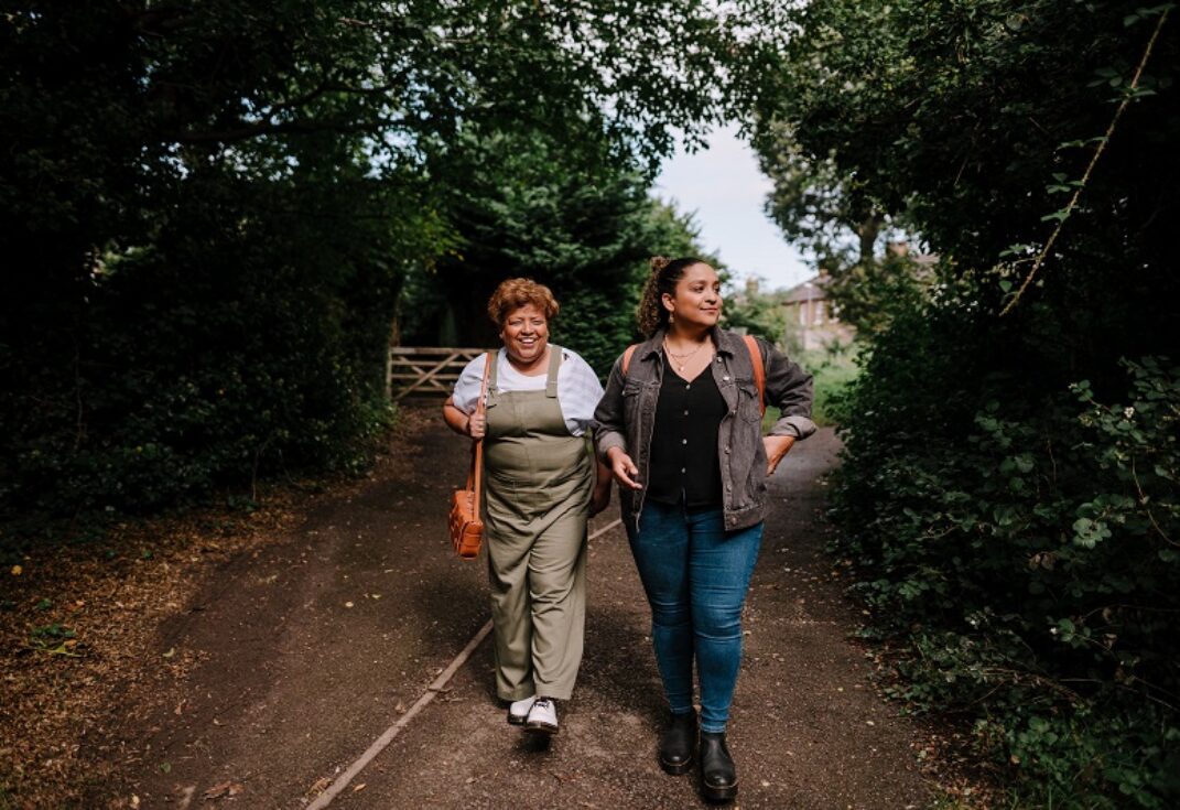 Two women walking along a path in a forest.
