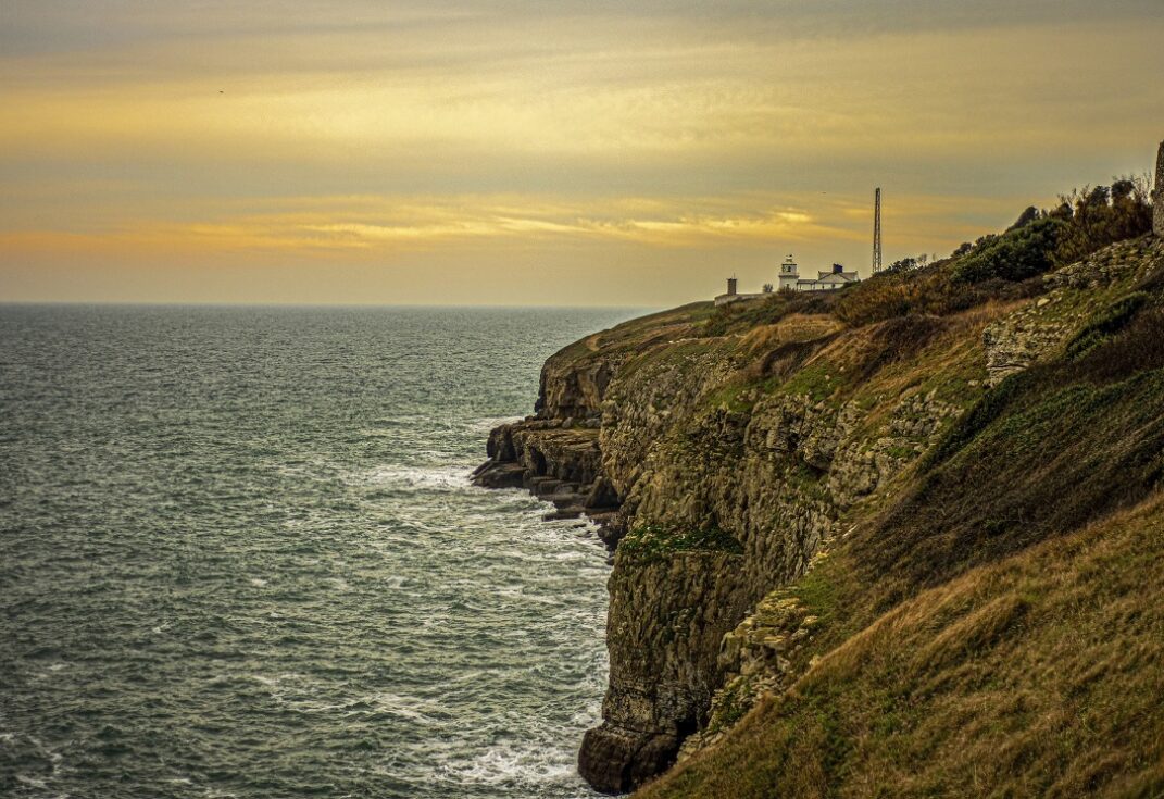Rocky cliff coastline with a small lighthouse in the distance and the sea below