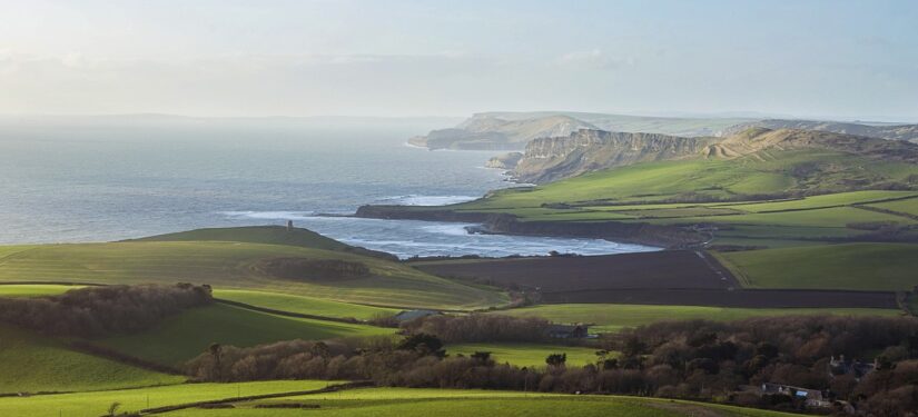A view of fields and sea with cliffs in the distance in bright sunshine