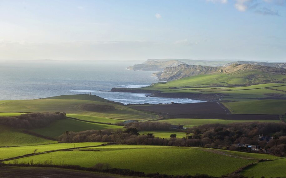 A view of fields and sea with cliffs in the distance in bright sunshine