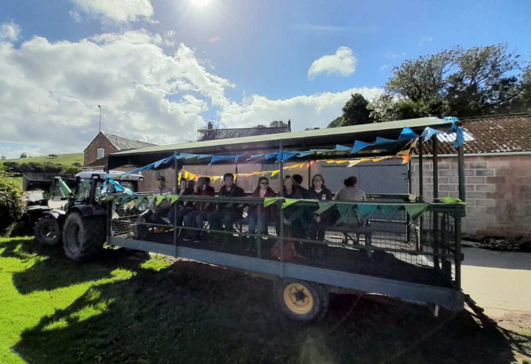 A group of people on a parked tractor and trailer on a sunny day.