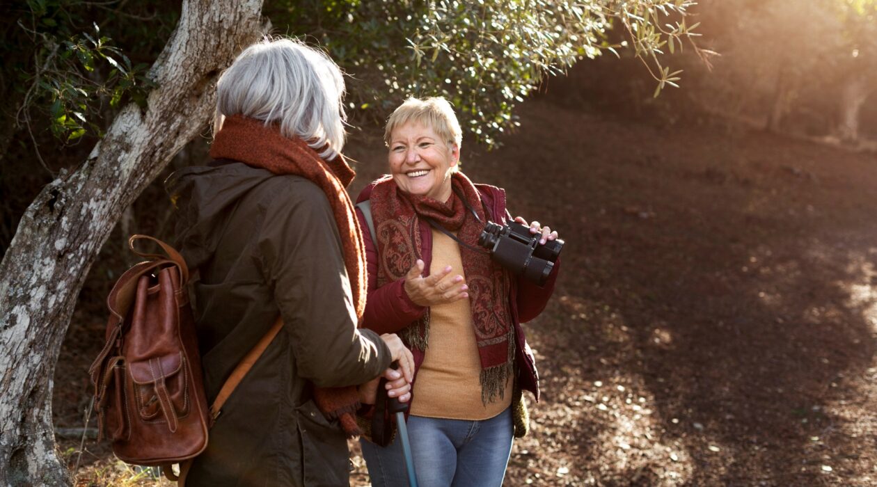 Two women enjoying time in a wood, one lady is holding binoculars and smiling.