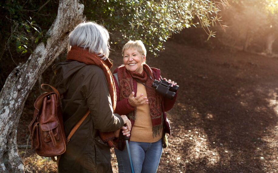 Two women enjoying time in a wood, one lady is holding binoculars and smiling.