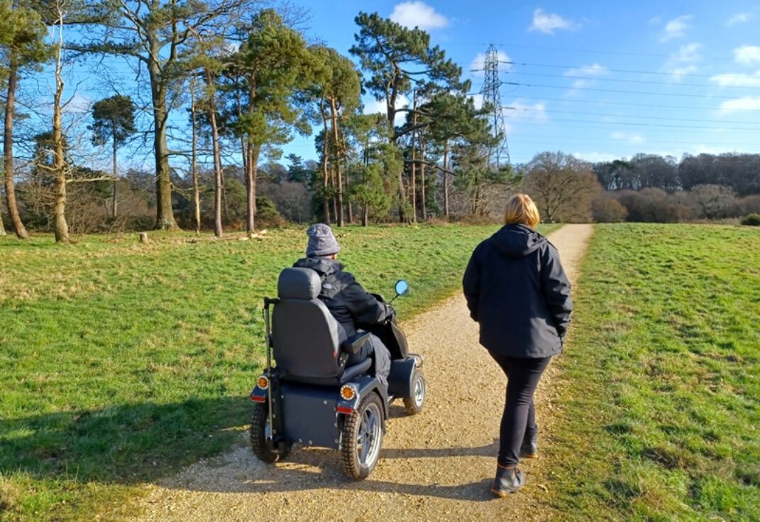 A woman walking beside a man on a tramper through a country park along a path on a bright day.