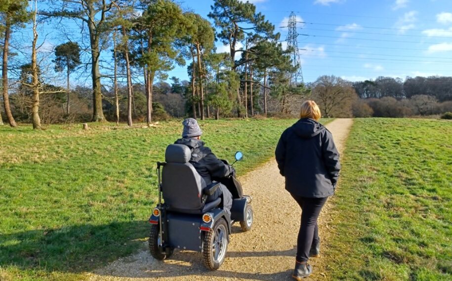 A woman walking beside a man on a tramper through a country park along a path on a bright day.