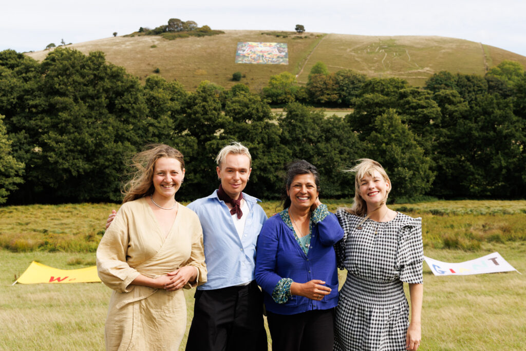 Four people smiling in foreground with giants on hillside in background