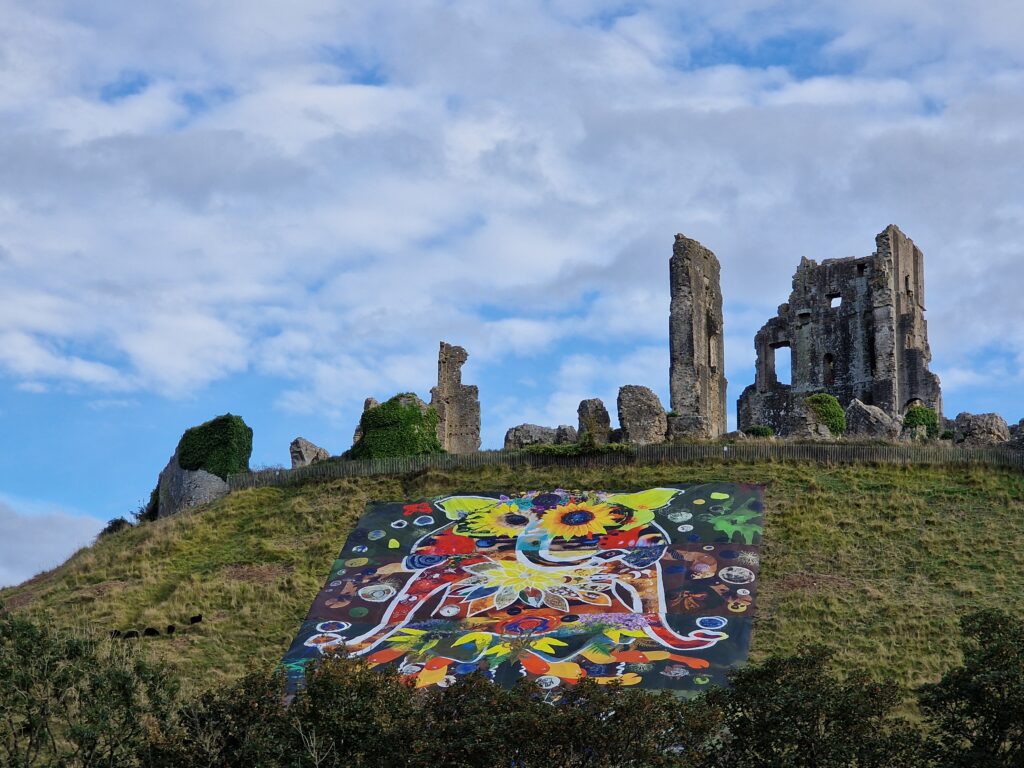Colourful artwork of Consequences Giant sits on hillside with ruined castle at the top of the hill