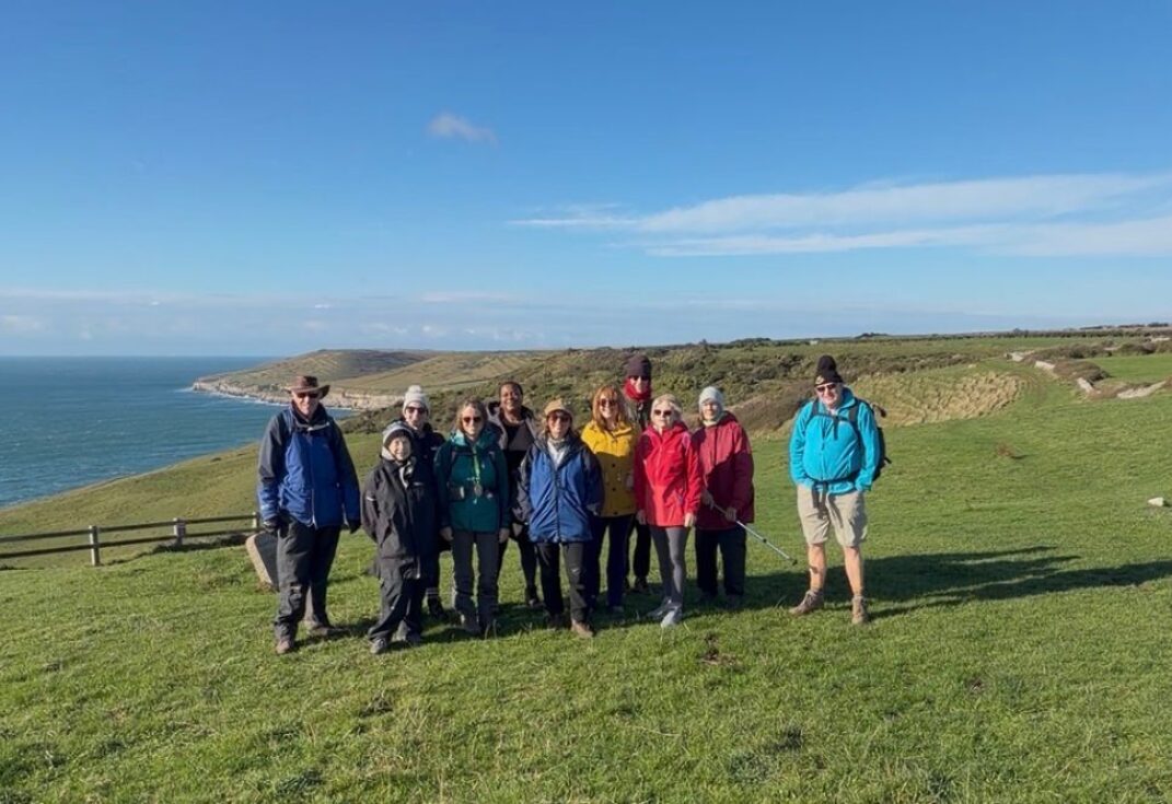A group photo of walkers on the coast path with the sea in the background on a bright winters day.