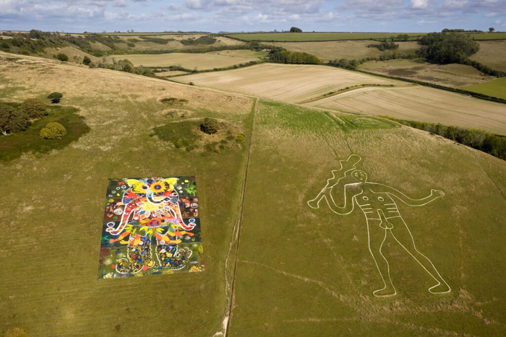 Green hillside with chalk Giant on right hand side and colourful artwork of new giant on left
