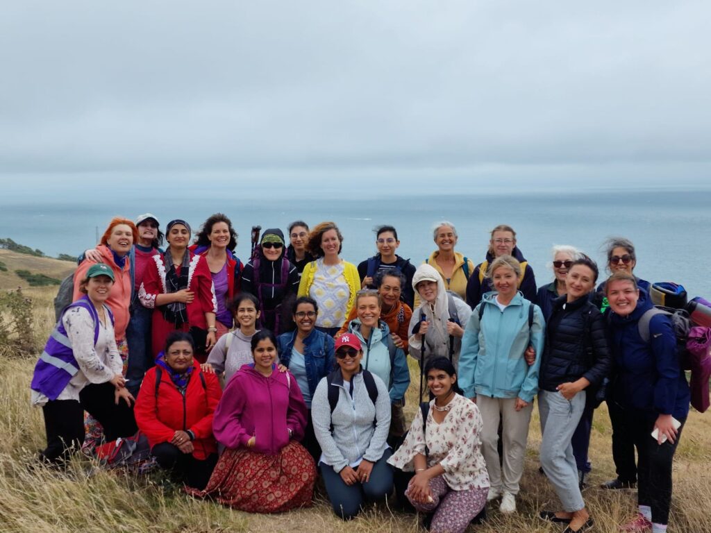 A group of people gathered on a coastal hillside, smiling toward the camera with the sea in the background under an overcast sky.