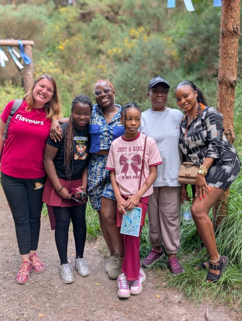 Six people stand together on a woodland path, posing for a group photo with trees and greenery behind them.