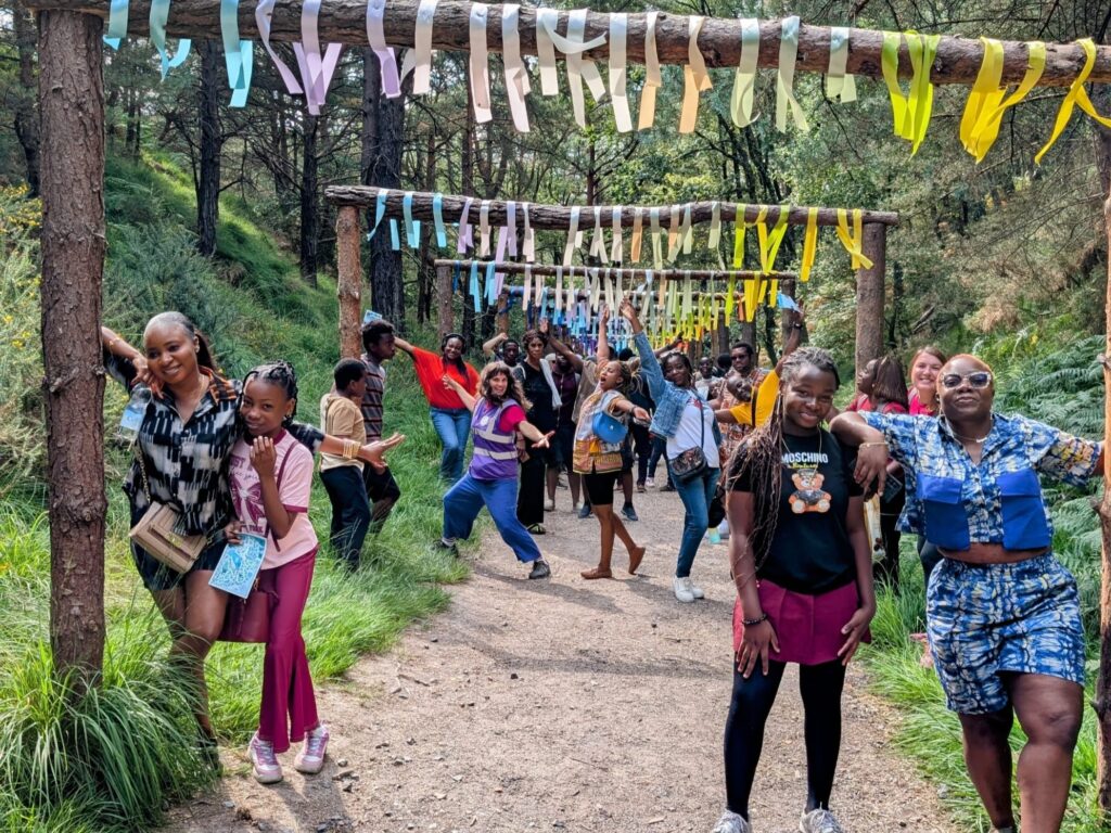 A large group poses along a forest trail under archways decorated with multicoloured ribbons.