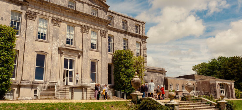 A large stately house with grand steps and people stood outside.