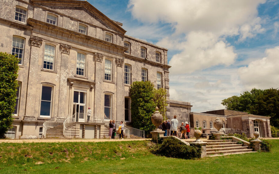 A large stately house with grand steps and people stood outside.