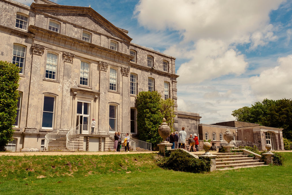 A large stately house with grand steps and people stood outside.